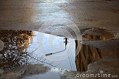 Reflection of the sky, the silhouette of a street lamp and a tree sunlit in a puddle on asphalt Stock Photo