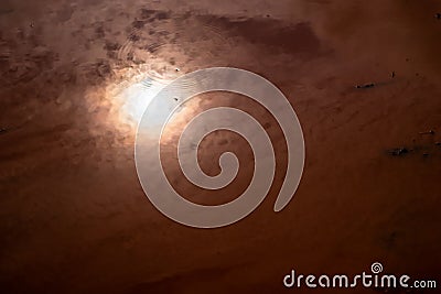 Reflection of the sun with orange bright light on a brown foggy and muddy swamp with ripples. Stock Photo