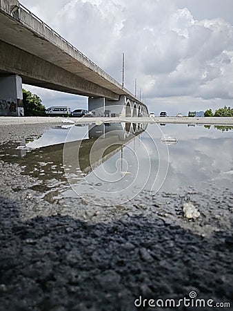 reflective pool of water on the asphalt street beneath the bridge crossing. Stock Photo