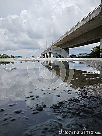 reflective pool of water on the asphalt street beneath the bridge crossing. Stock Photo