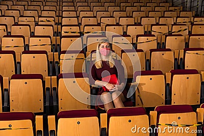 Reflective woman in protective mask sitting alone in empty cinema house Stock Photo