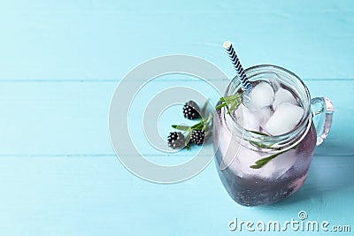 Refreshing blackberry drink with rosemary and ice cubes in mason jar on turquoise wooden table. Space for text Stock Photo