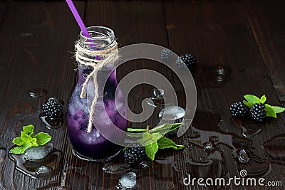 Refreshing blackberry juice in vintage eco style bottle on rustic dark wooden table. Cold summer berry drink with ice and mint Stock Photo