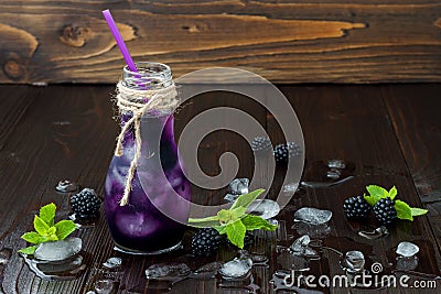 Refreshing blackberry juice in vintage eco style bottle on rustic dark wooden table. Cold summer berry drink with ice and mint. Co Stock Photo
