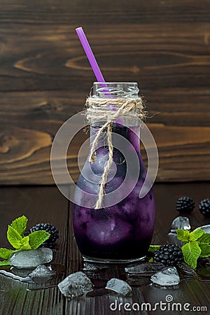 Refreshing blackberry juice in vintage eco style bottle on rustic dark wooden table. Cold summer berry drink with ice and mint. Co Stock Photo