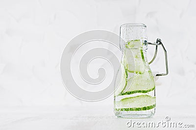 Refreshing cold detox drink with green cucumber, bright bubbles in transparent yoke bottle in elegant white interior on wood table Stock Photo