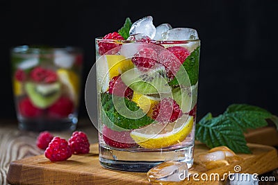 Refreshing drink with mineral water, with berries and fruits raspberry, lemon, kiwi and ice on a black background. Stock Photo