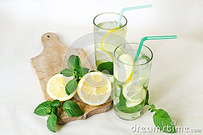 Refreshing water with lemon, mint leaves and ice in glass glasses with colored tubules. Lemon with mint branches on a wooden board Stock Photo