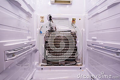 Refrigerator repair. Freezer compartment back panel removed. Evaporator coils with a frozen thermostat Stock Photo