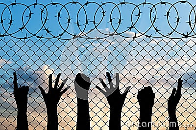 Refugees hands silhouette near the fence of barbed wire. Stock Photo