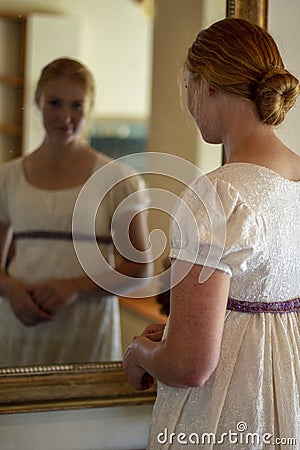 Regency woman in cream dress looks in a gold framed mirror Stock Photo