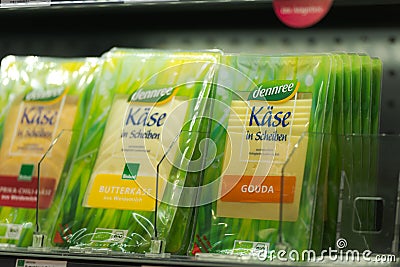 Regensburg, Germany - 2021 02 05: Refrigerated section with packs of different sliced cheese of brand dennree behind glass doors Editorial Stock Photo