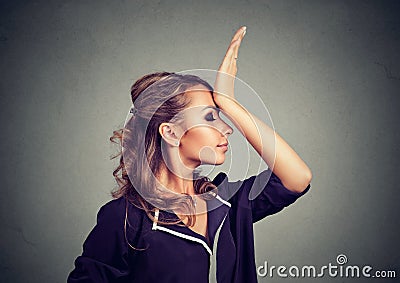 Regrets wrong doing. Sad woman, slapping hand on head having duh moment isolated on gray background. Stock Photo