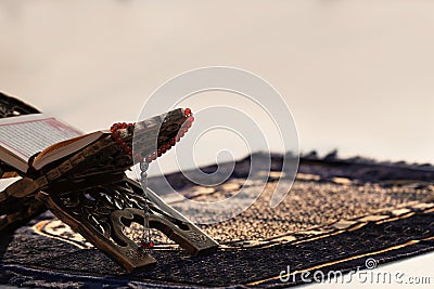 Rehal with open Quran and Muslim prayer beads on rug Stock Photo