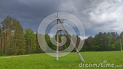 A reinforced concrete pole of a power line with electric wires stands in a meadow near the forest. A thunderstorm is coming from b Stock Photo
