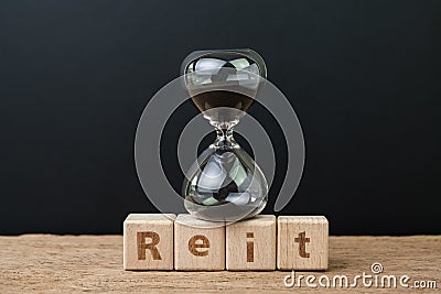 REIT, Real estate investment trust booming time concept, sandglass or hourglass on wooden cube block with alphabet building the Stock Photo