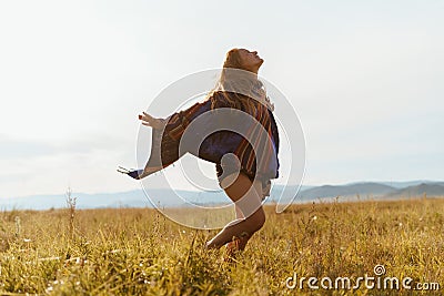 rejoices in the warm wind and runs to meet him on the steppe grass girl in shorts and ethno cape. red hair harmonizes Stock Photo