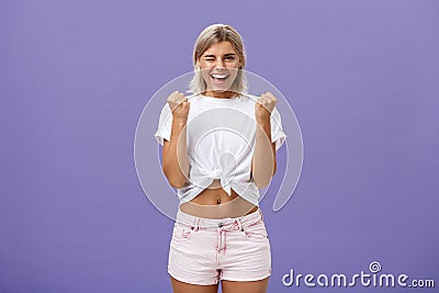 Rejoicing satisfied and pleased happy young ambitious girl with blonde hair in trendy white cropped top and shorts Stock Photo