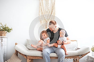 Kitchen in bright colors. Relationship in the family with young children and father. Dad hugs two daughters on the couch in the br Stock Photo