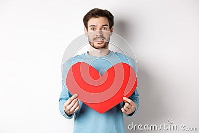 Relationship and love concept. Handsome caucasian man in sweater holding big red valentines day heart cutout and smiling Stock Photo