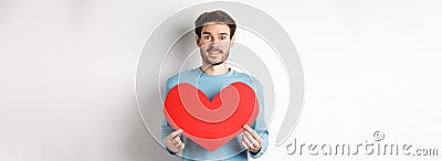 Relationship and love concept. Handsome caucasian man in sweater holding big red valentines day heart cutout and smiling Stock Photo