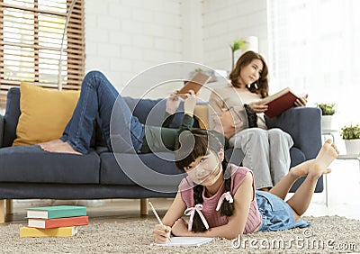 Relax Asian parent reading a book on sofa and daughter painting art in living room at home Stock Photo