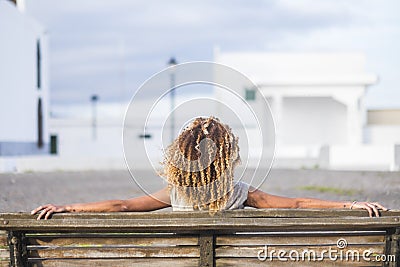 Beautiful curly hair black skin tanned woman viewed from back sitting on a bench Stock Photo