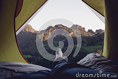 Relax woman lying down and cross leg on blanket in tent and looking at mountain view in sunset time at camping vacation holiday Stock Photo