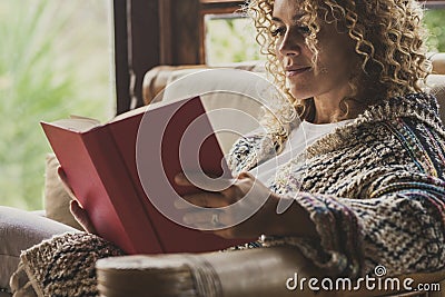 Relaxed adult lady reading a book sitting on the chair at home with outside view. Concept of female people happy lifestyle living Stock Photo