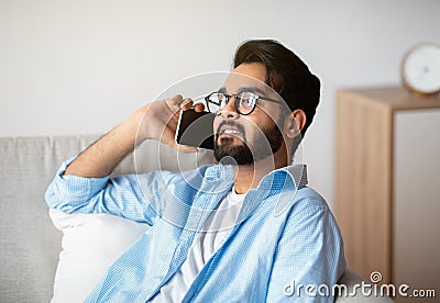 Relaxed Arab Man Talking On Celphone While Resting On Couch At Home Stock Photo