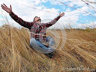 Relaxed calm man stretches out his hands to the sky while sitting in nature. Relaxation and mindfulness. Stock Photo