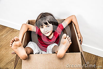 Relaxed child sitting in old cardboard box with feet out Stock Photo