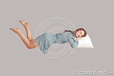 Relaxed girl in vintage ruffle dress levitating in mid-air, sleeping on stomach lying comfortable cozy on pillow Stock Photo