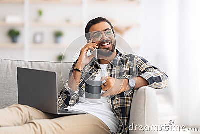 Relaxed guy sitting on sofa with laptop, having phone coversation Stock Photo