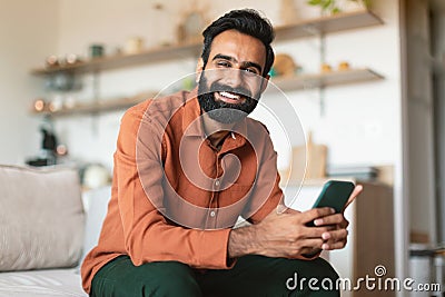 Relaxed Indian Guy Using Smartphone Resting On Couch At Home Stock Photo