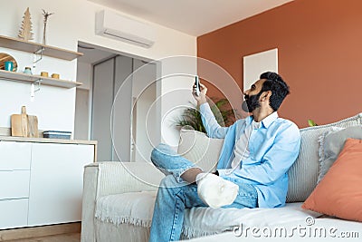 Relaxed Indian Man Turning On Air Conditioner Sitting At Home Stock Photo