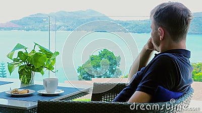 A relaxed man enjoys his lunch break in a hotel cafe terrace with a sea view. Stock Photo