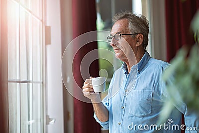 Relaxed mature man at home standing by the window Stock Photo