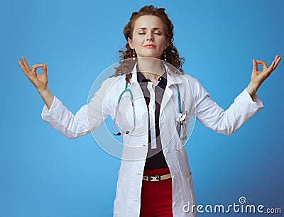 Relaxed modern physician woman doing yoga on blue Stock Photo