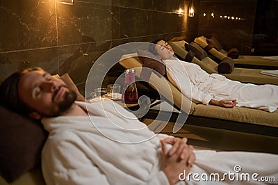 Relaxed newlywed, beautiful heterosexual married couple lying down on chaise lounge with closed eyes, spending time together, Stock Photo