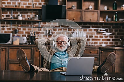 Relaxed old man in headphones using laptop with feet Stock Photo