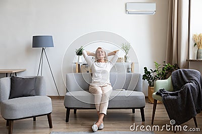 Relaxed older woman sitting on couch in air conditioner room Stock Photo