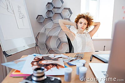 Relaxed pensive curly young woman photographer sitting on workplace Stock Photo
