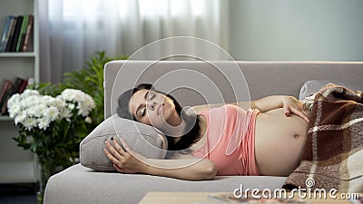 Relaxed pregnant lady sweetly sleeping on sofa, hugging her tummy with baby Stock Photo