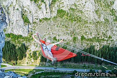 Relaxed tourist male in a hammock high up in a mountain, above the valley, secured with a via ferrata set on two steel wires Stock Photo