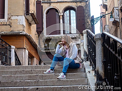 Relaxed tourist woman sitting on the stairs on a bridge in the city of Venice, Italy Stock Photo