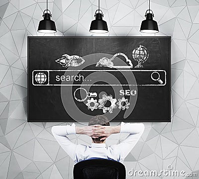 Relaxing businessman is looking at the chalkboard with the drawn internet search bar and different icons. Stock Photo