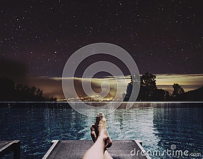Relaxing in holidays, a man feet on bed at swimming pool at night with city lights and stars on sky background Stock Photo