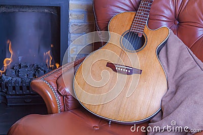 Relaxing winter hobbies. Acoustic guitar on armchair by the fire Stock Photo