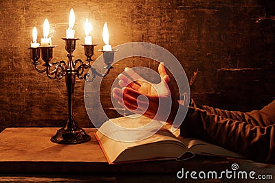 Religious female crossed hands in prayer with bible and candle Stock Photo